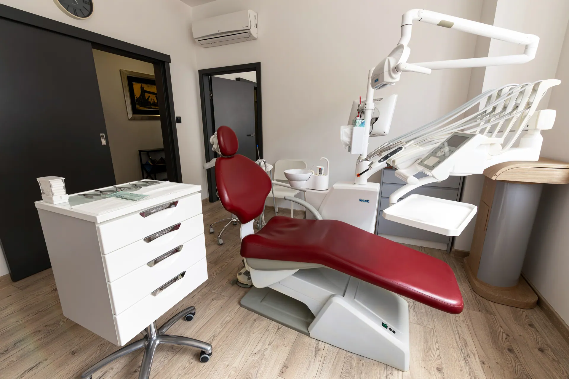 Orto-vis treatment room with a burgundy dental chair and a modern dental unit.
